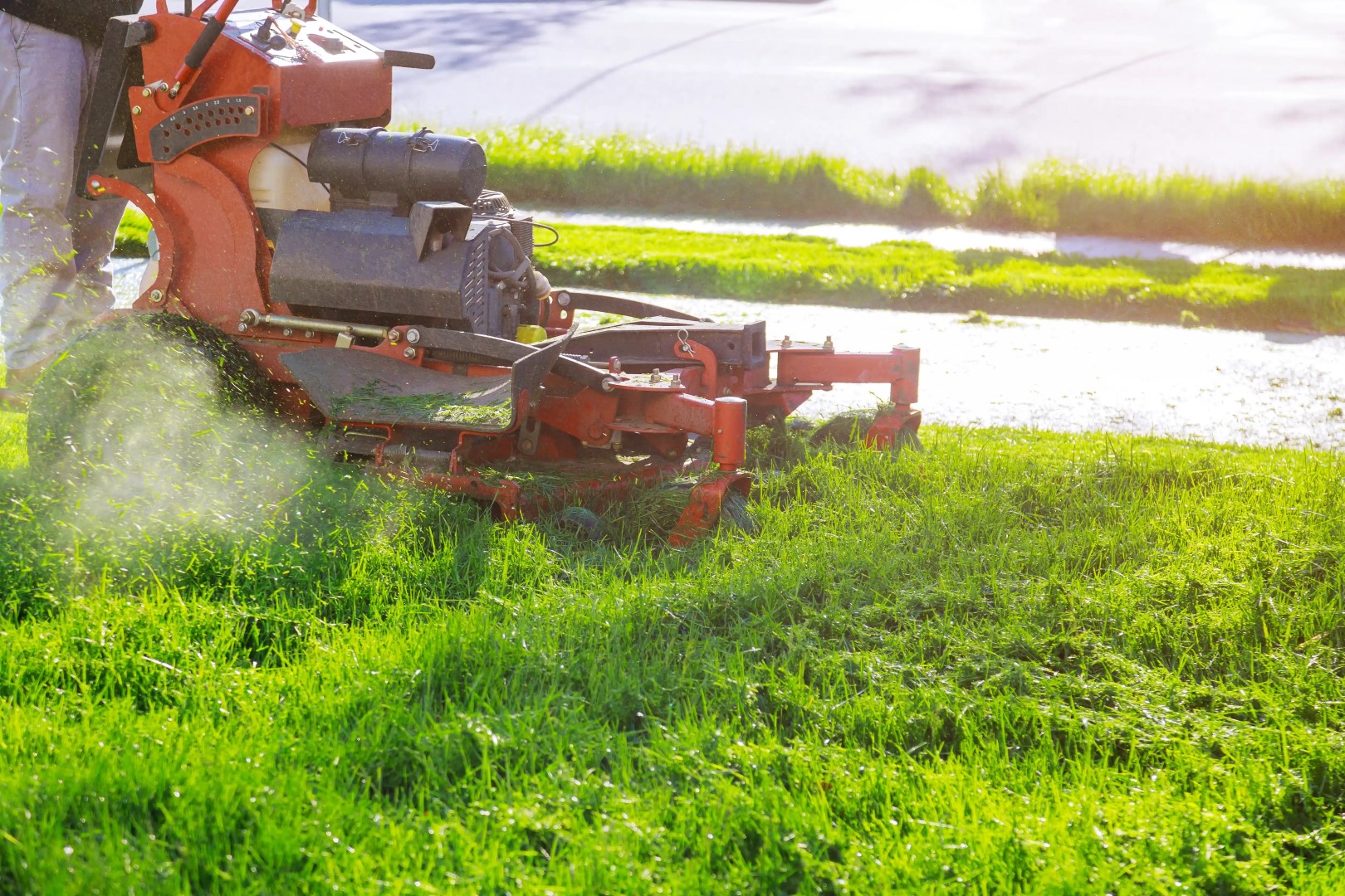 A person operates an orange lawn mower cutting vibrant green grass on a sunny day in Winter Haven. The freshly cut lawn contrasts with the uncut grass, exemplifying fast lawn care. Sunlight filters through, creating a bright and lively atmosphere.